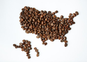 Closeup above view shot: heap of rich brown freshly roasted coffee seeds scattered on white table in shape of world map with continents