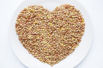 Above view of ripe lentil seeds laid out on white porcelain plate in shape of heart