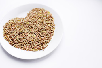 Closeup shot of ripe lentil seeds laid out in shape of heart on white porcelain plate