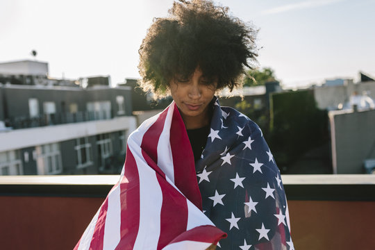 Young woman standing on rooftop wrapped in US American flag
