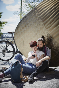 Germany, Hamburg, couple on bicycle trip having a rest looking at cell phone