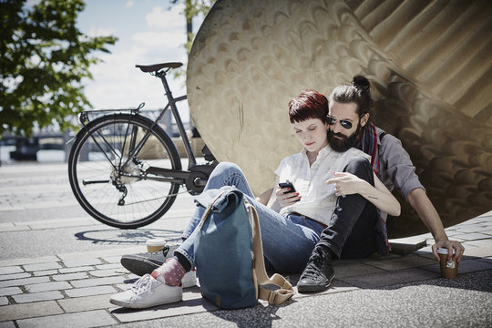 Germany, Hamburg, couple on bicycle trip having a rest looking at cell phone