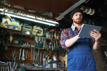 Low angle portrait of handsome mechanic using tablet to check auto systems in repair workshop