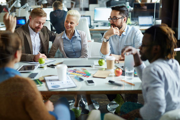 Creative group of designers sitting in boardroom with glass wall and sharing ideas concerning new project in relaxed atmosphere, two of them wearing green slippers