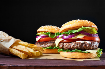 Two craft beef burgers and french fries on wooden table isolated on black background.