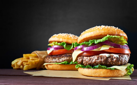 Two craft beef burgers and french fries on wooden table isolated on black background.