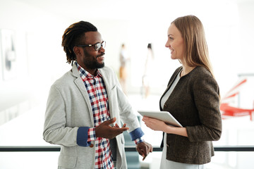 Smiling business partners standing in office lobby and discussing details of their agreement, silhouettes of workers observed on background