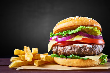 Craft beef burger and french fries on wooden table isolated on black background.