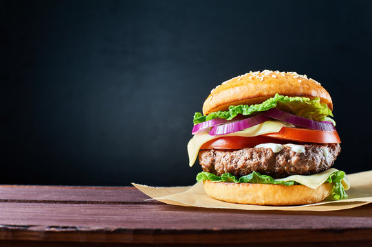 Craft beef burger on wooden table isolated on dark blue background.