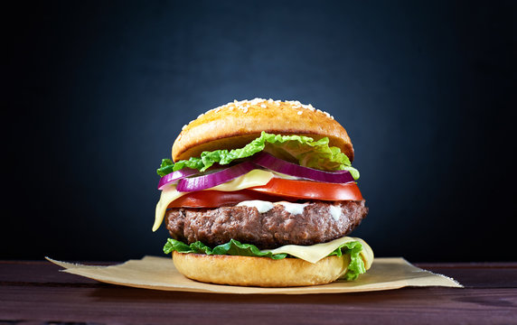 Craft beef burger on wooden table isolated on dark blue background.