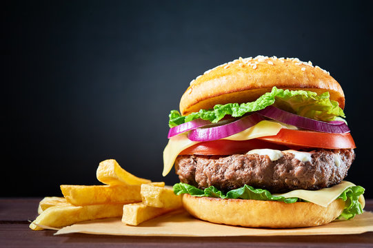 Craft beef burger and french fries on wooden table isolated on dark blue background.