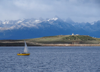 Small boat sailing on quiet lake with surrounded by snow-capped mountains