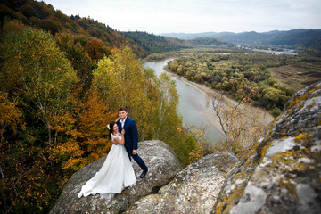 beautiful and young bride and groom standing on big stone