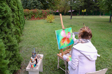 Professional artist woman writes picture sitting at easel with b
