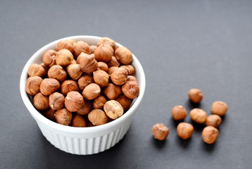 White bowl of hazelnuts. Black background
