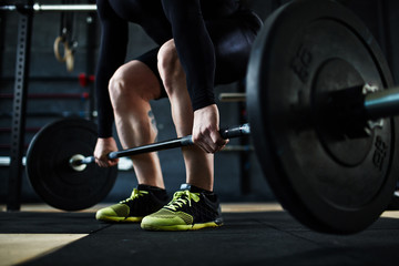 Low section of unrecognizable male athlete lifting huge heavy barbell from floor, leg muscles straining with effort - Powered by Adobe