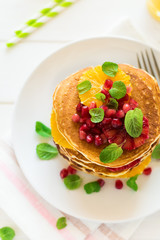 Traditional breakfast: stack of pancakes with orange slices and pomegranate seeds decorated mint leaves on white wooden table. Selective focus