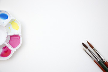 Obraz premium A watercolor dish palette filled with paints and brushes placed on blank white paper as background