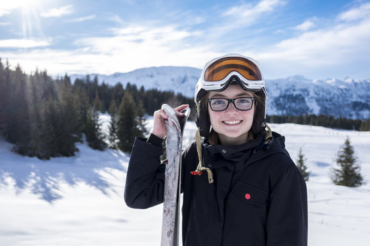 Young girl, posing with skis, on the side of a piste, in Meribel, in the French Alps.  The day is clear, with a deep blue, sunny sky, and the girl is wearing ski clothes