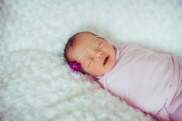 Newborn baby yawns sleeping in violet blanket on bed