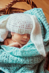 Fototapeta na wymiar Tiny girl in white hat sleeps in mint blanket in a basket