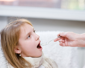 Teen girl taking medicine with spoon