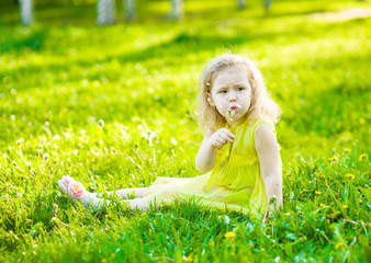 Little girl blowing dandelion on green grass