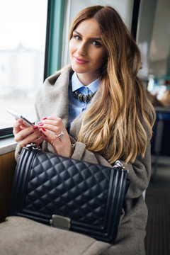 Beautiful young woman sitting in city bus and typing a message on the phone. 