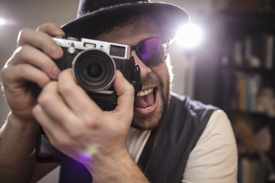 happy smiling photographer hipster wearing sunglasses and hat taking pictures using old style retro camera