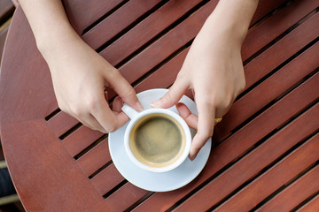 woman hands with espresso coffee on a wood table.