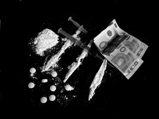 Injection syringe on cocaine drug powder lines, cocaine pile and pills and euro money bills on black background in black and white colors