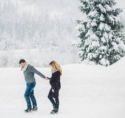 Pregnant lady holds man's hand walking with him around winter forest