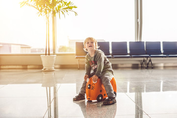 Cute little boy with orange suitcase at airport