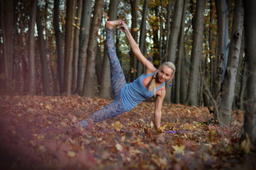 Young blond woman with braid doing yoga asanas in autumn forest.
