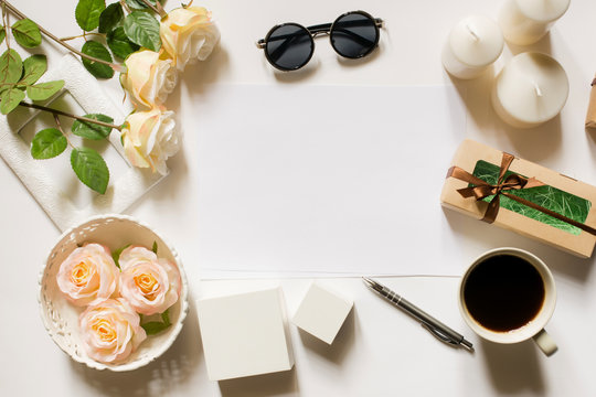 Empty sheet with copy space on the white desk with coffee cup, sunglasses, roses, pen, gifts, candles and vintage white tray. Top view, flat lay, copyspace.