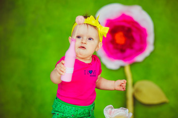 Curious child with yellow bow on her head looks at ball in pink bottle