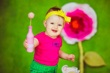 Girl in pink shirt laughs reaching out her little hand with pink bottle