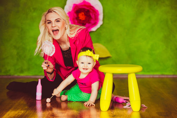 Mom in pink jacket and little girl with yellow bow on her head play on the floor