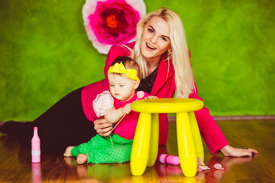 Mother And Daughter Have Fun Sitting Before Yellow Chair In Green Room