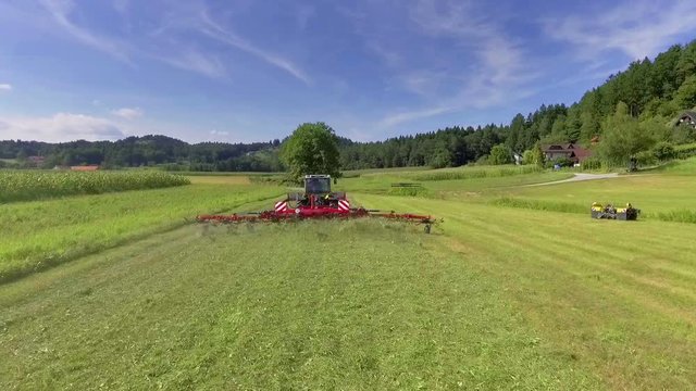 A tractor is preparing hay on a beautiful field in the countryside. It is summer time and the nature looks fabulous.
