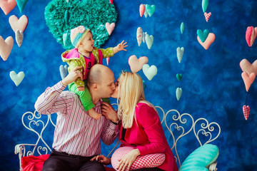 Young man and woman in pink clothes kiss holding their little daughter