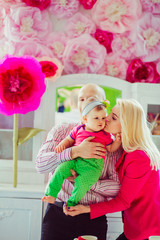 Mother in pink jacket kisses little girl tender standing in pink room