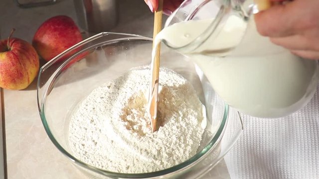 Pouring milk into flour. Whisking milk and flour in a glass bowl. Slow motion.