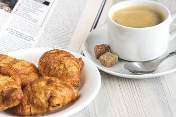 french breakfast with coffee, croissants, newspaper on a light wooden background
