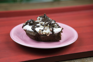 Piece of chocolate cake on pink small saucer over red painted wooden surface, close-up side view