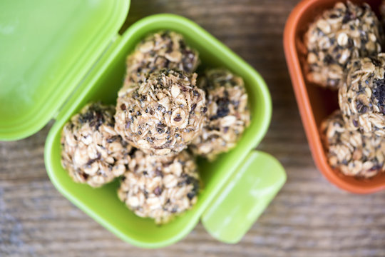 Homemade granola ball candies in plastic containers close-up over wooden table