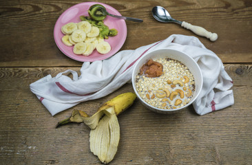 Oatmeal with milk and cashew nuts in white bowl on wooden table with banana and kiwi fruit, healthy breakfast concept