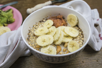 White ceramic bowl of muesli in milk with banana slices, close-up view with white towel on wooden table