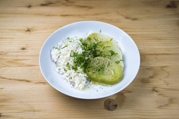 Close-up dish of rice with cabbage slices and herbs on white plate on unpainted wooden table