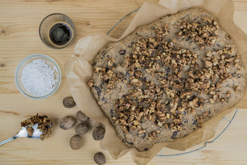Cake with roasted walnuts on baking paper with nuts in shells and ingredients over wooden table surface